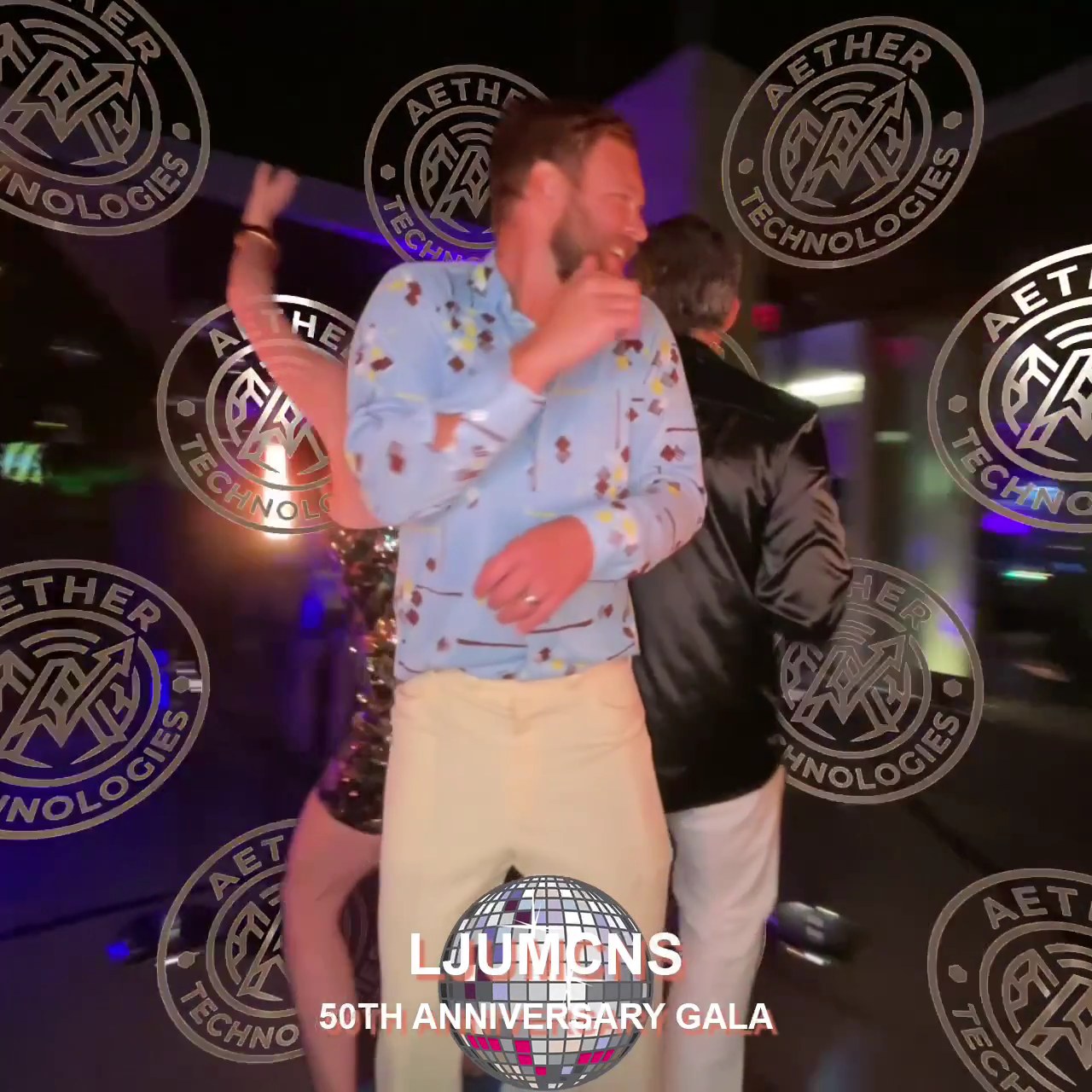 A guest in a patterned shirt dancing on the platform at night with a ring of round Aether Technologies demo logos rendered behind him and an LJUMONS 50th Anniversary Gala overlay below