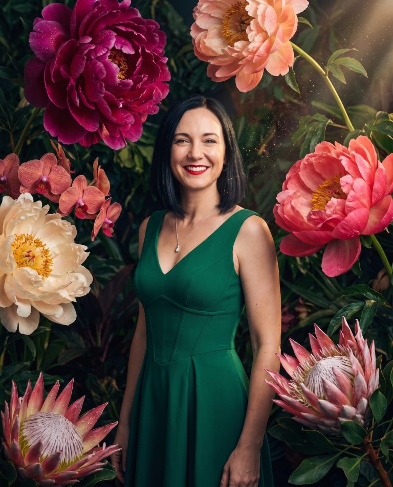 A guest standing among impossibly enormous peonies and ranunculus that tower far above their head.