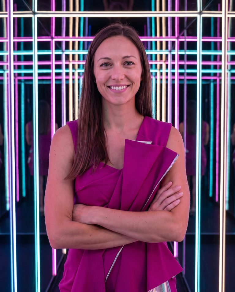 A guest stands inside a mirrored infinity enclosure lined with continuous LED strips.