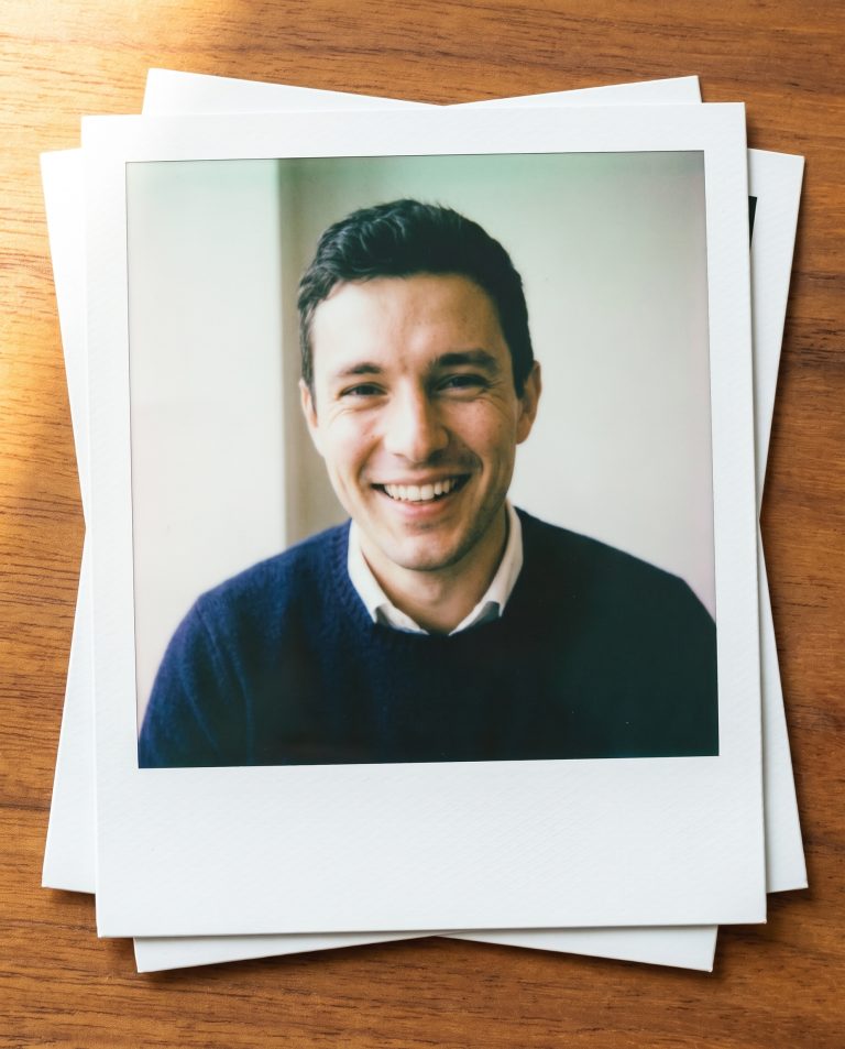 A guest pictured inside a single instant-film print resting on a loose stack of blank prints.