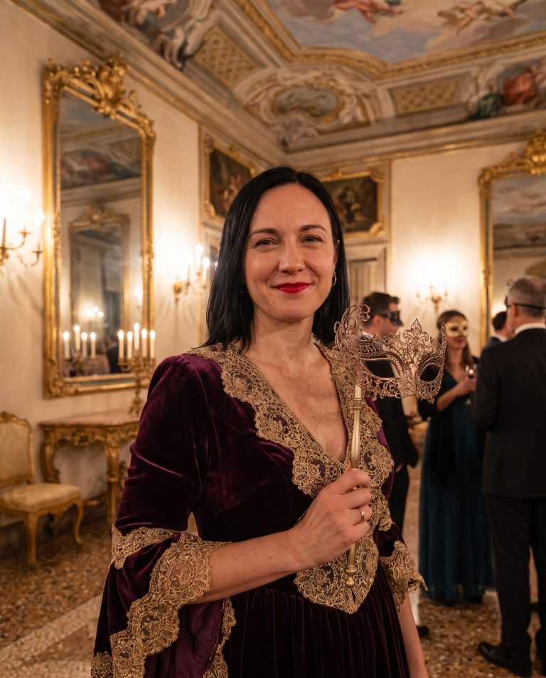 A guest stands in a candlelit Venetian palazzo ballroom at midnight, gilded baroque mirrors.