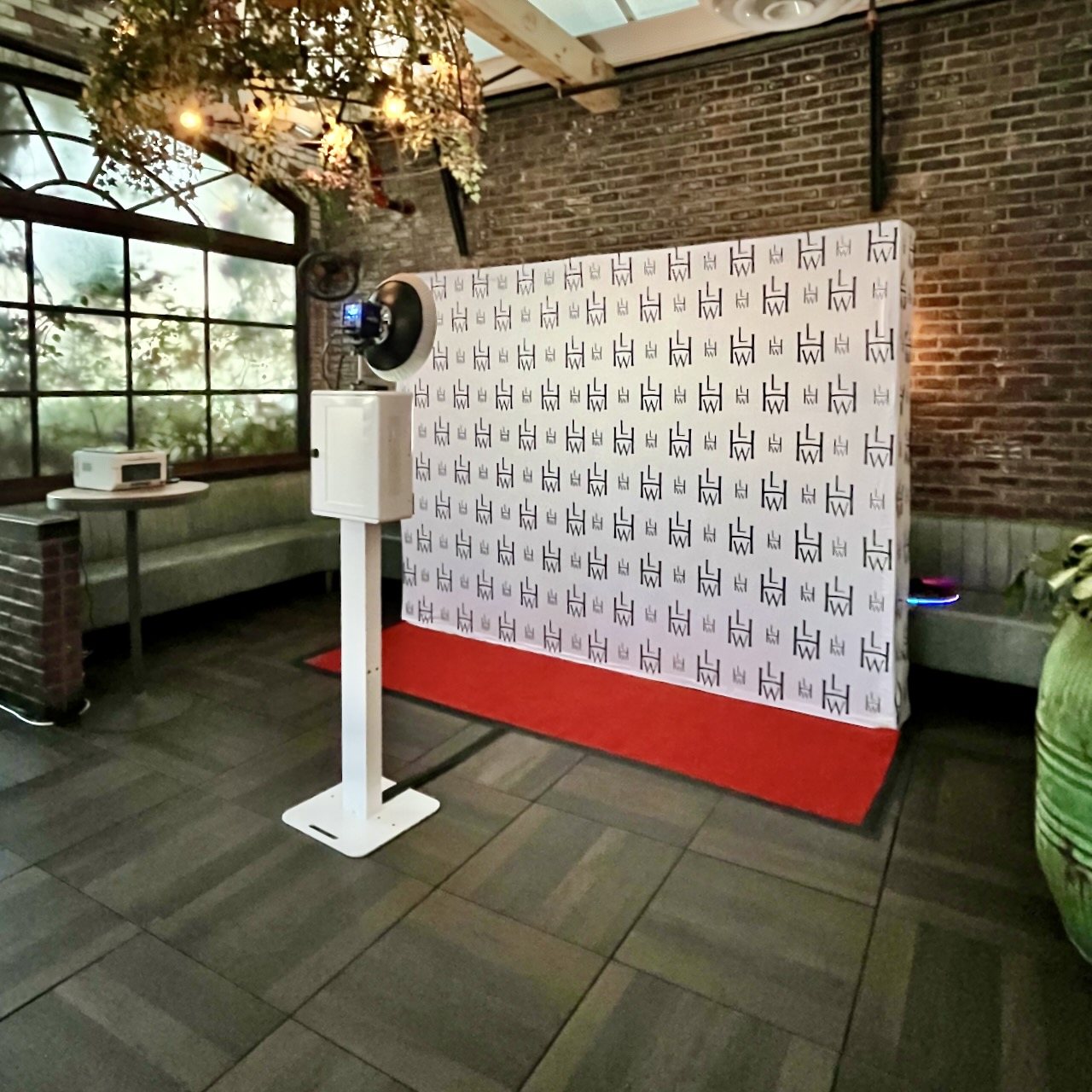 A white booth on a stand with a ring light facing a printed step-and-repeat wall of Leading Hotels of the World logos, with a red carpet in front of it in a brick-walled venue
