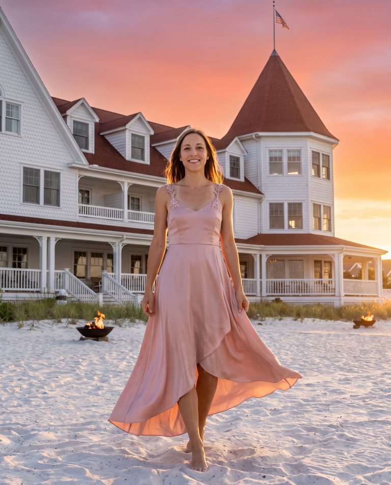 A guest stands on wide white sand at sunset with a grand Victorian beachfront resort rising behind them.