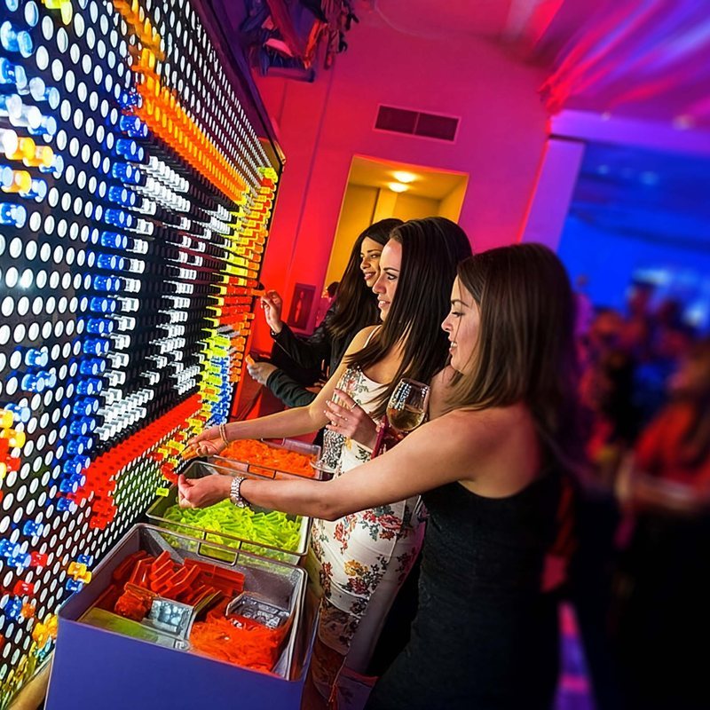 Guests pressing colored light pegs into a giant glowing peg wall at an evening reception