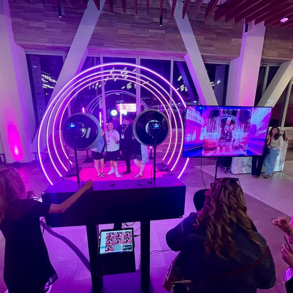 Guests pose inside glowing rings at a camera array while an operator runs the station at an evening company event