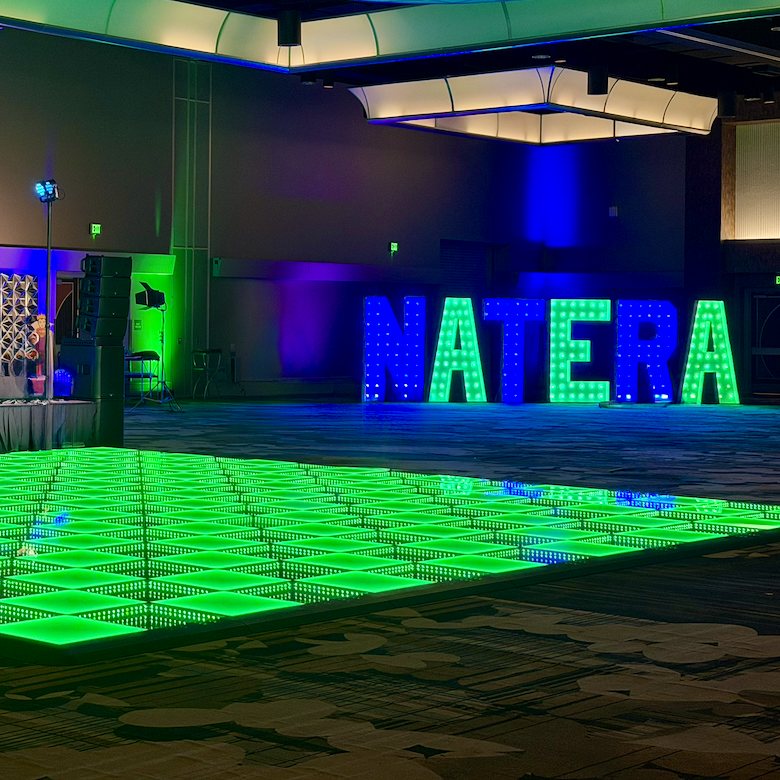 A lit green LED floor filling a hotel ballroom, with tall lit letters and a stage behind it