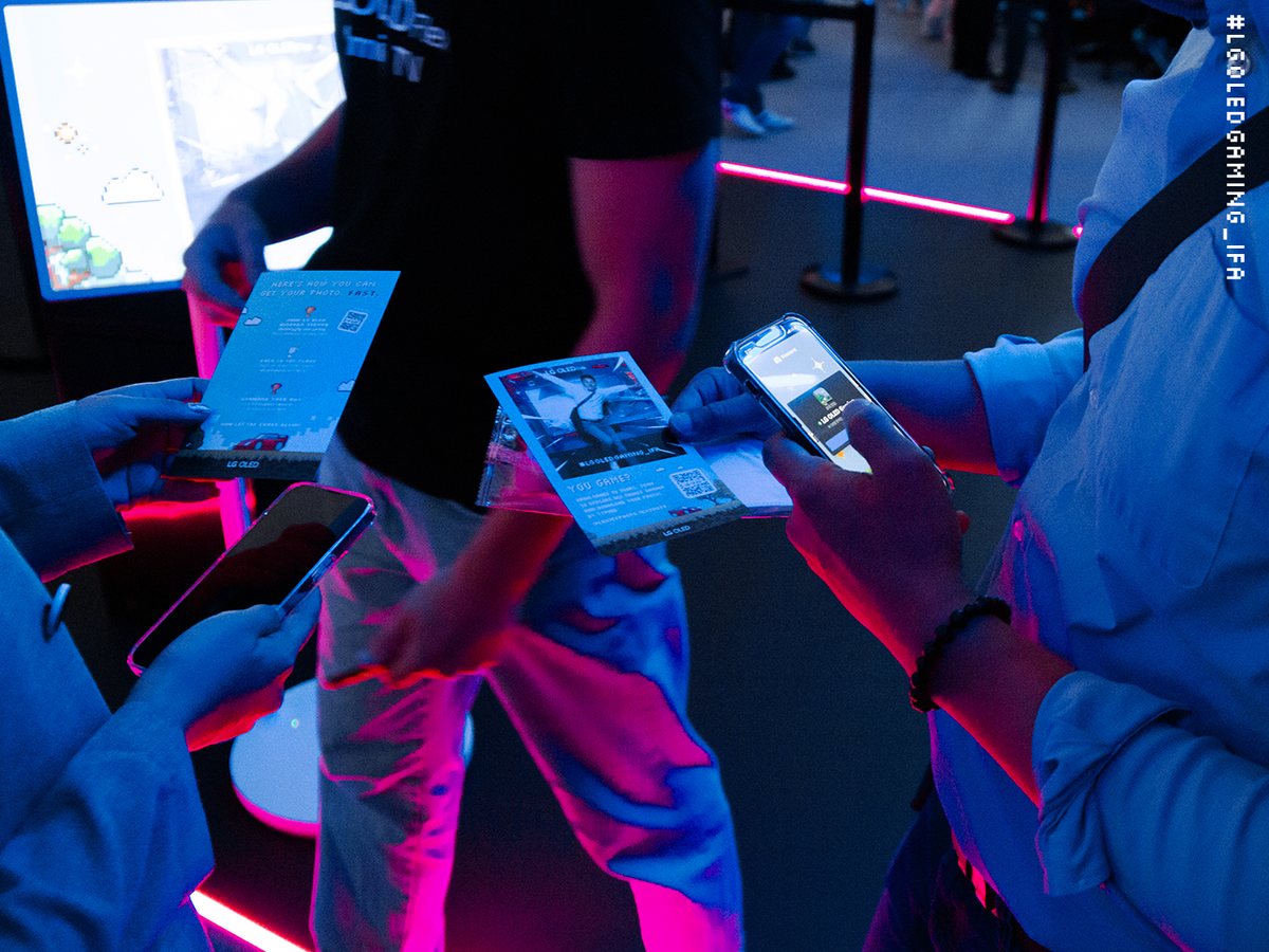 Guests hold printed photo cards and phones under pink and blue light