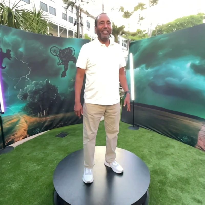 A guest on a 360 platform in front of a curved printed backdrop on a hotel lawn with the Hotel del Coronado behind