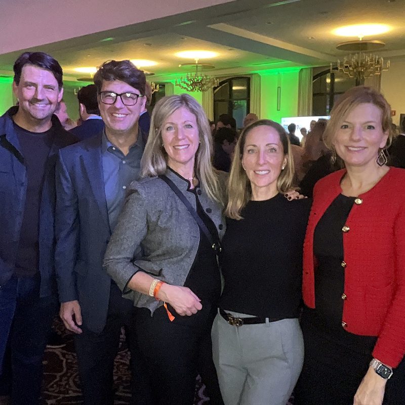 Five guests in business attire posing for a roaming photographer in a ballroom lit green and purple